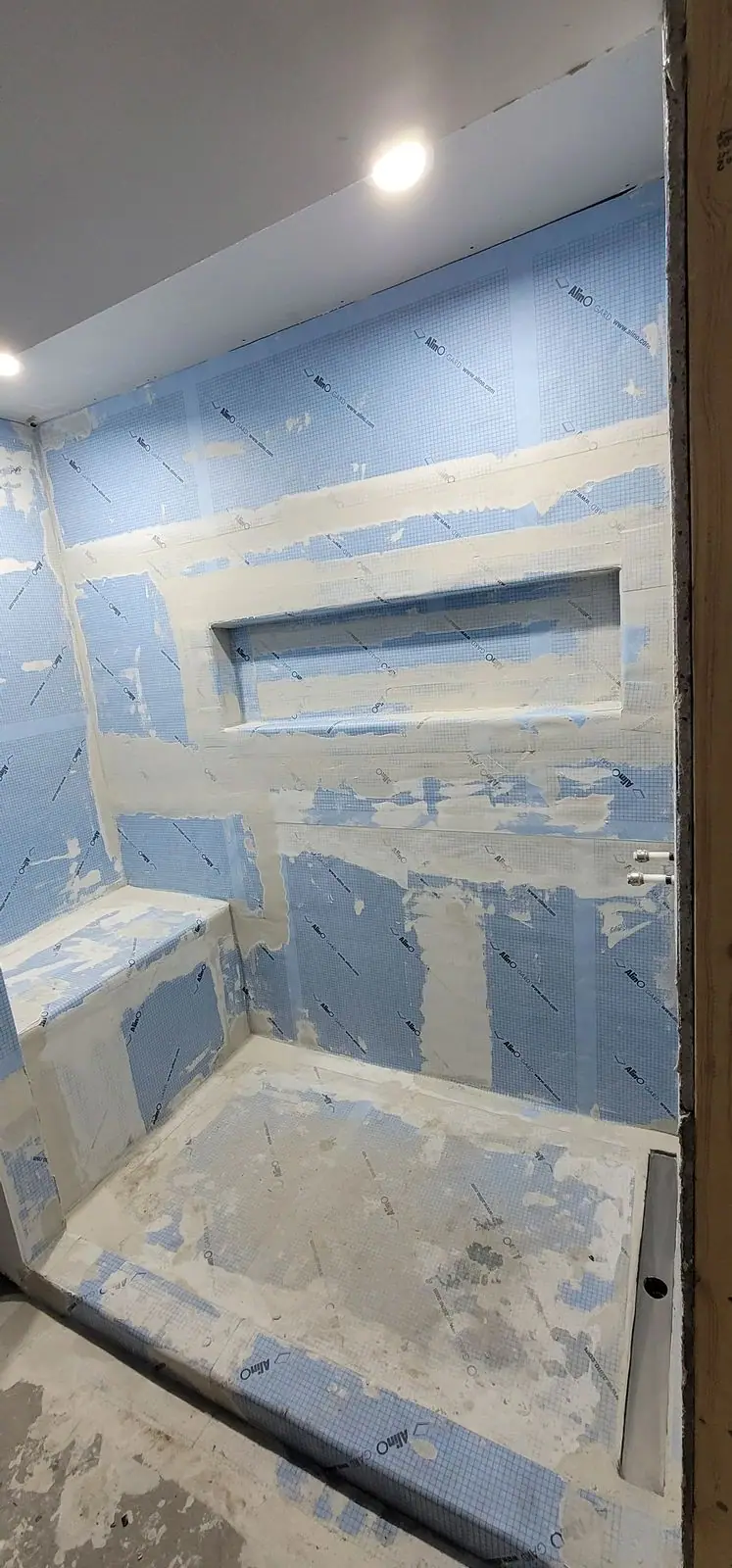 A shower with the waterproofing membrane on and the bench and niche formed, before tile